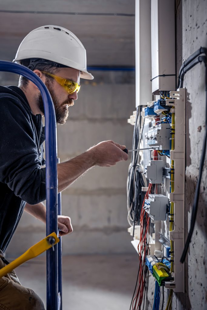 A male electrician works in a switchboard with an electrical connecting cable.